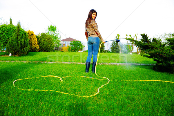 Back view portrait of a smiling woman is watering grass in her garden Stock photo © deandrobot