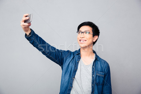 Smiling young asian man making selfie photo Stock photo © deandrobot