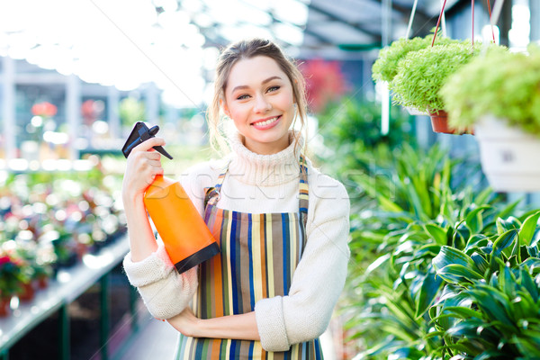 Cheerful attractive woman gardener standing in orangery with water pulverizer Stock photo © deandrobot