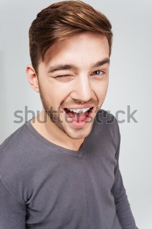 Stock photo: Happy attractive young man in grey pullover winking 