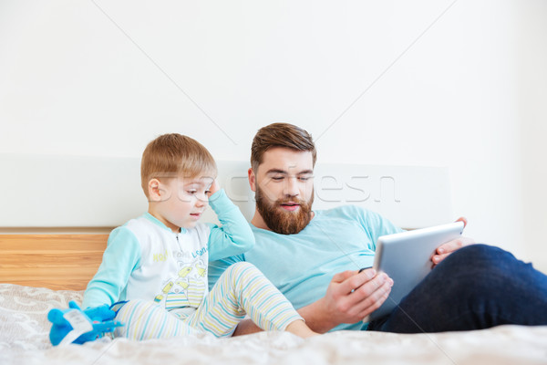 Stock photo: Father and son using tablet lying on bed 