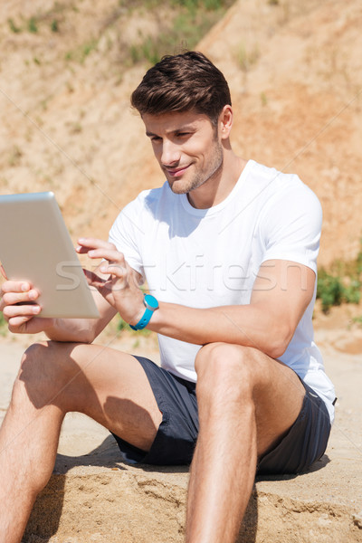 Souriant jeune homme comprimé plage séance affaires [[stock_photo]] © deandrobot