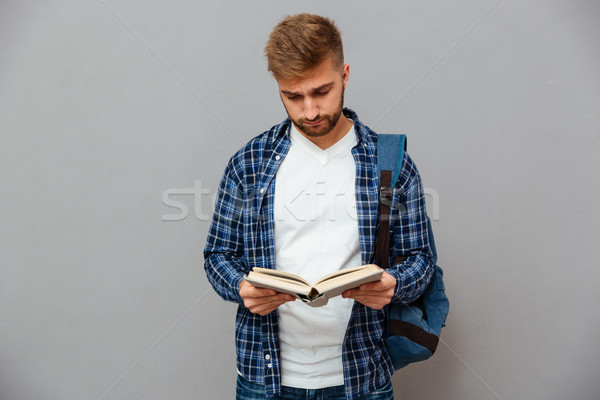 Stock photo: Handsome bearded man in checkered shirt with backpack reading book