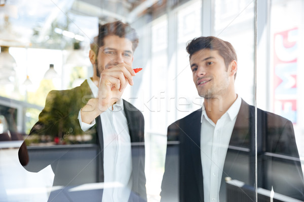 Two happy businessmen writing on glass board in office Stock photo © deandrobot