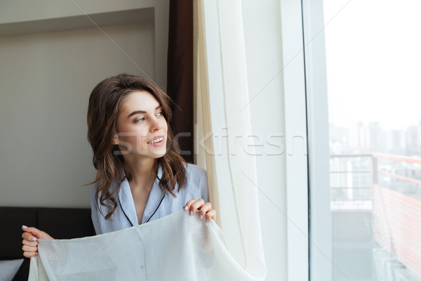Portrait of a happy woman opening window curtains Stock photo © deandrobot