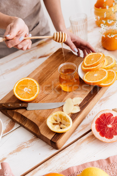 Woman standing near table with citruses and holding honey. Stock photo © deandrobot