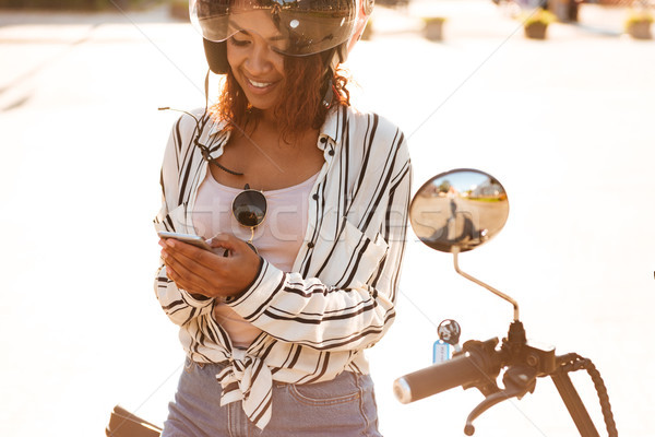 Smiling african woman sitting on modern motorbike outdoors Stock photo © deandrobot