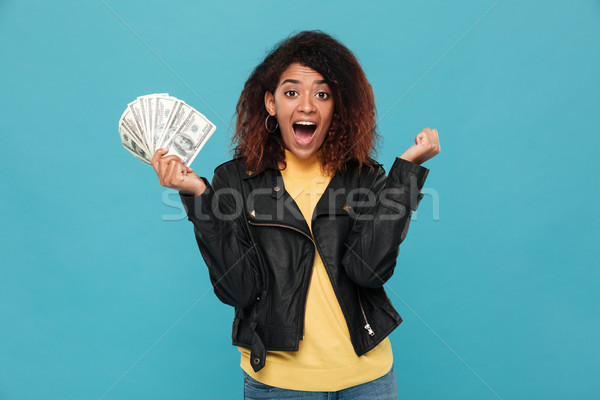 Surprised happy african woman in leather jacket holding money Stock photo © deandrobot