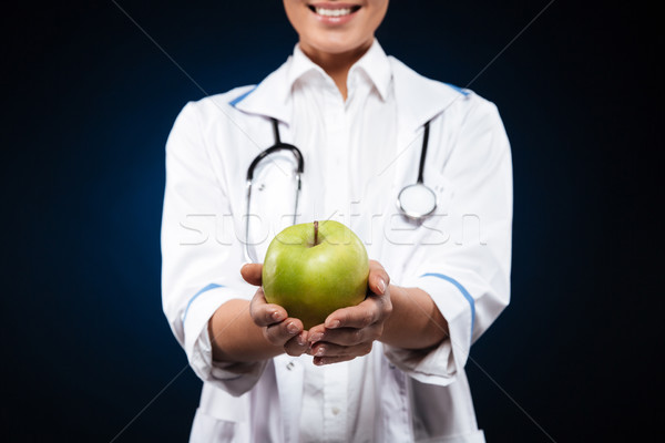 Cropped photo of young woman in medical gown holding green apple Stock photo © deandrobot