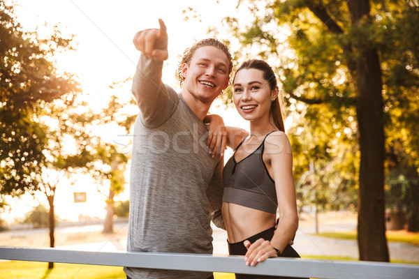Fitness sport loving couple friends in park outdoors looking aside while pointing. Stock photo © deandrobot