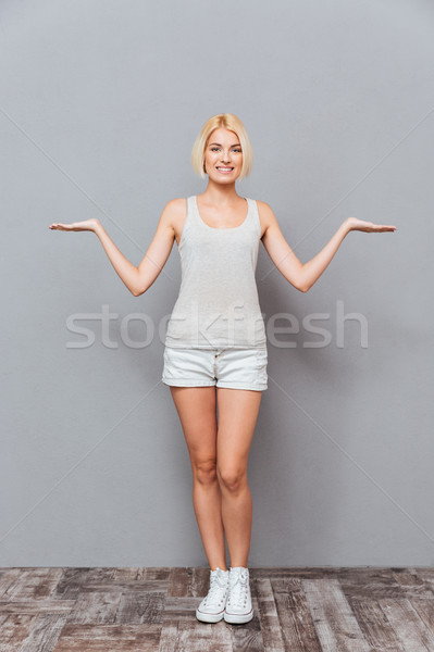 Cheerful young woman standing and holding copyspace on both palms Stock photo © deandrobot