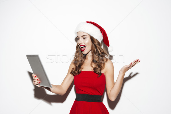 Happy pretty young woman in santa claus costume using tablet Stock photo © deandrobot