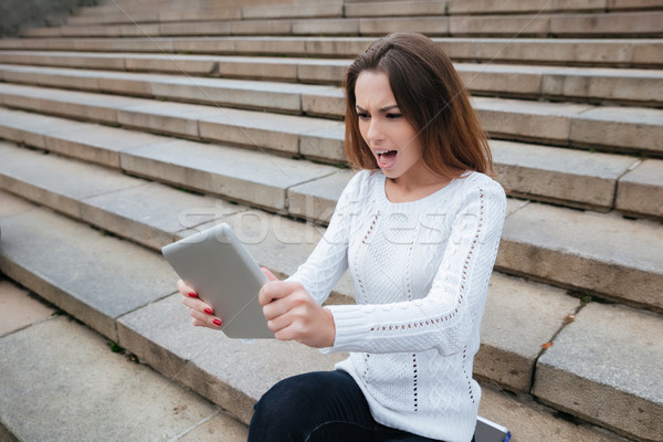 Angry woman sitting on stairs and using tablet Stock photo © deandrobot
