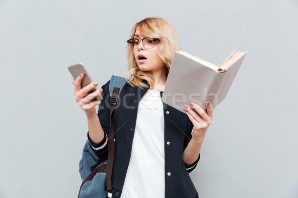 Shocked young woman using phone and holding book. Stock photo © deandrobot