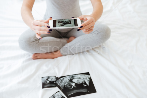 Pregnant woman taking pictures of ultrasound photos with cell phone Stock photo © deandrobot