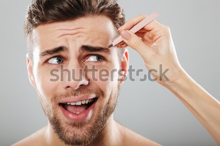 Beauty portrait of a young man plucking eyebrows with tweezers Stock photo © deandrobot