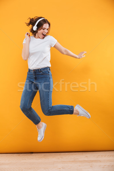 Emotional funny young woman jumping listening music. Stock photo © deandrobot