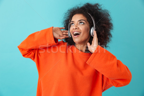 Attractive american woman in orange shirt enjoying music via wir Stock photo © deandrobot