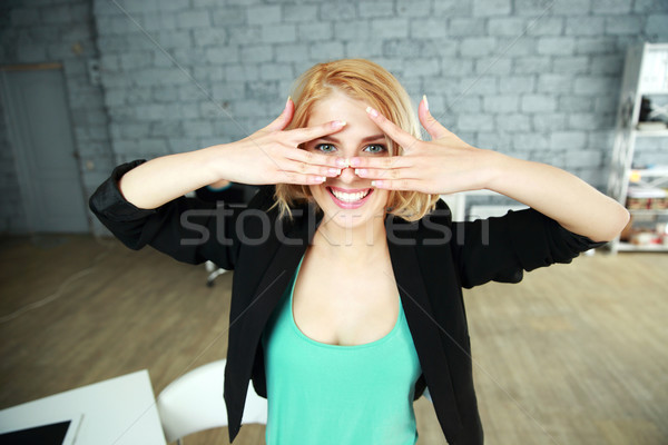 Young cheerful woman looking through fingers at camera in office Stock photo © deandrobot