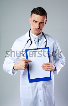Confident male Doctor standing with clipboard over white background Stock photo © deandrobot