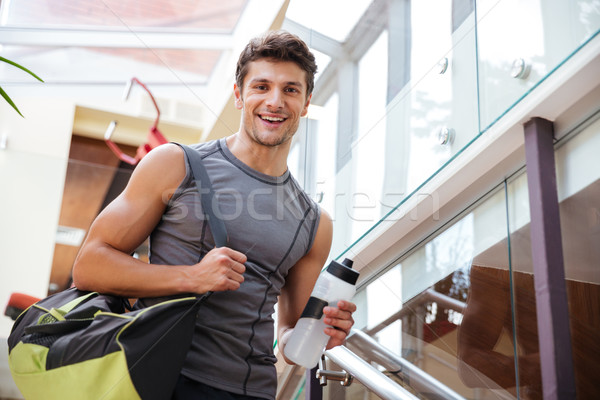 Cheerful fitness man with bottle of water walking on training Stock photo © deandrobot