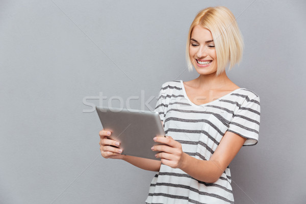Uśmiechnięty cute młoda kobieta blond włosy tabletka szary Zdjęcia stock © deandrobot