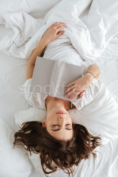 Tired young woman with book lying and sleeping in bed Stock photo © deandrobot
