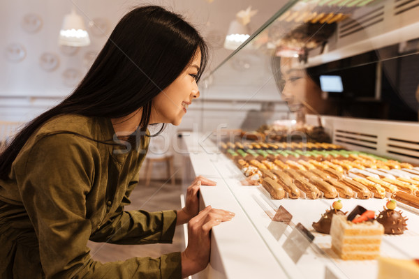 Cheerful asian young lady looking at sweeties. Stock photo © deandrobot