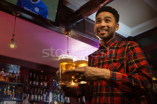 Smiling afro american man carrying glasses of beer Stock photo © deandrobot