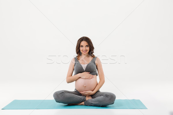 Happy pregnant woman sitting on fitness mat and holding tummy Stock photo © deandrobot