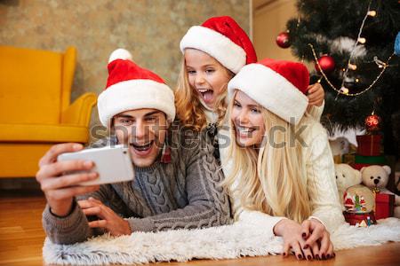 Happy little girl in Santa's hat makes horns to her parents whil Stock photo © deandrobot