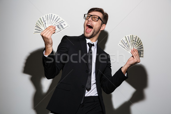 Overjoyed bearded man in black suit holding two bunches of dolla Stock photo © deandrobot