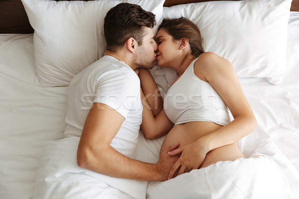 Happy pregnant woman lies in bed with her husband kissing. Stock photo © deandrobot