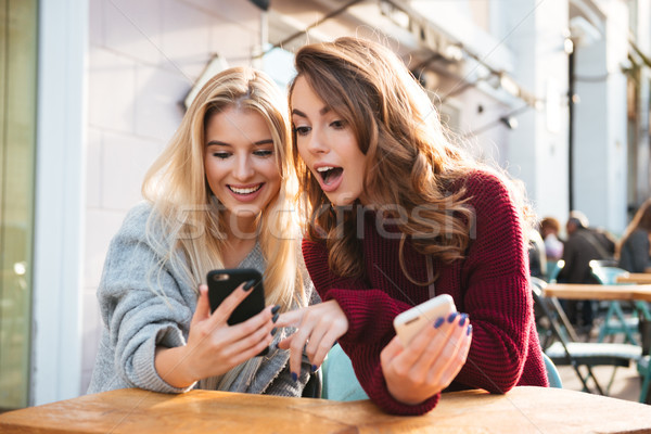 Kettő izgatott fiatal lányok mobiltelefonok ül Stock fotó © deandrobot