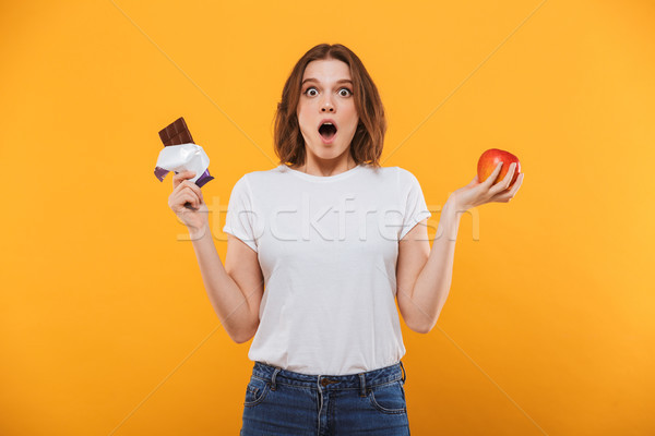 Emotional young woman holding apple and chocolate. Stock photo © deandrobot