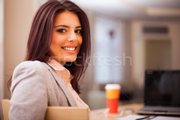 Young businesswoman sitting at desk and working. Smiling and looking back at camera Stock photo © deandrobot