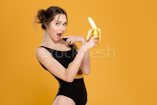 Surprised lovely cute young woman in black swimwear holding banana  Stock photo © deandrobot