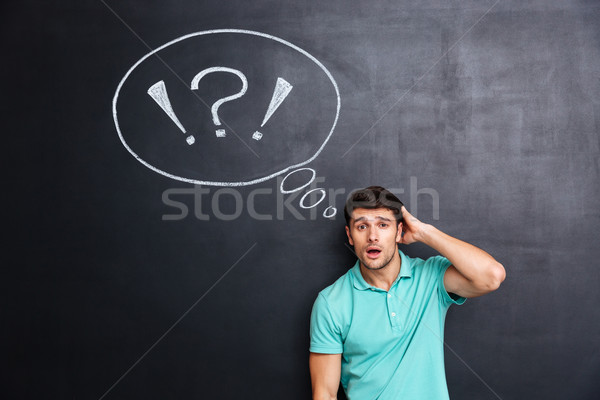 Puzzled confuzed young man over chalkboard background Stock photo © deandrobot