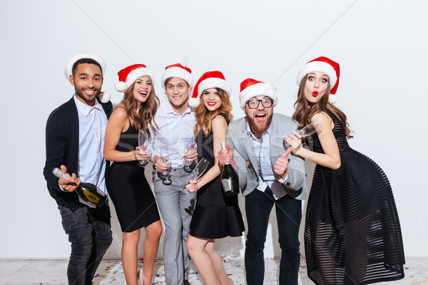 Cheerful friends in santa claus hats holding bottle of champagne Stock photo © deandrobot