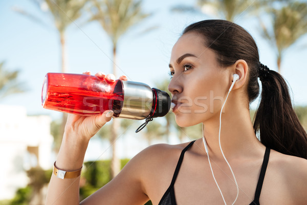 Attractive young woman athlete with earphones drinking water in summer Stock photo © deandrobot