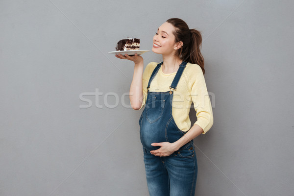 Happy pregnant lady holding sweet cake. Looking aside. Stock photo © deandrobot