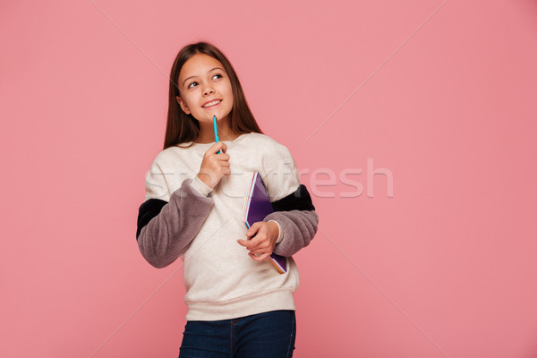Smiling girl looking up and thinking while holding pencil and books Stock photo © deandrobot