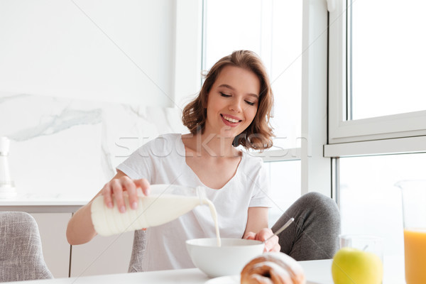 Portrait of a smiling young woman pouring milk Stock photo © deandrobot