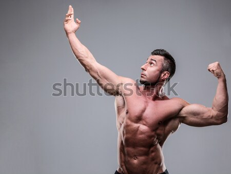 Portrait of a muscular man with raised hands up over gray background Stock photo © deandrobot
