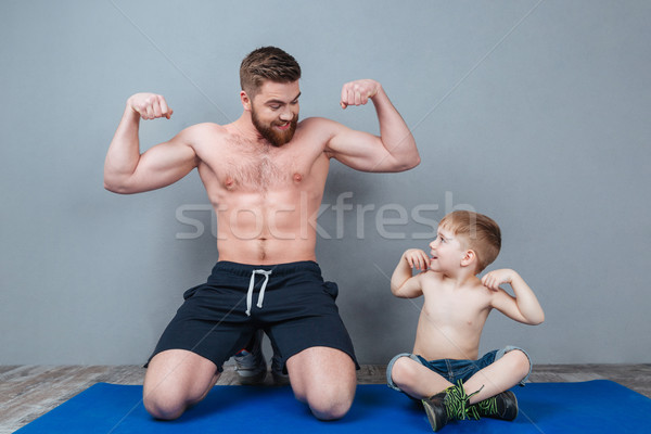 Smiling shirtless dad and son showing biceps sitting on mat Stock photo © deandrobot