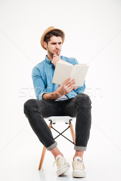 Concentrated young man in hat sitting and reading a book Stock photo © deandrobot