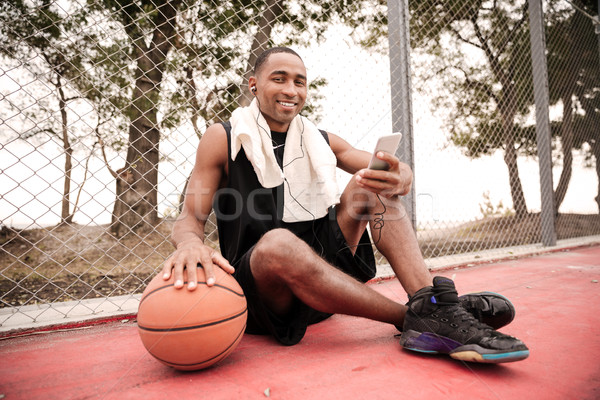 Cheerful african basketball player sitting with towel while list Stock photo © deandrobot