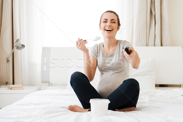 Cheerful pregnant woman with ice cream laughing and watching TV Stock photo © deandrobot
