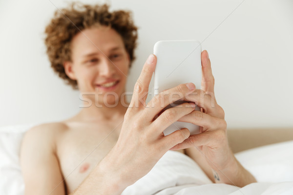 Cheerful handsome man lies in bed chatting by phone Stock photo © deandrobot