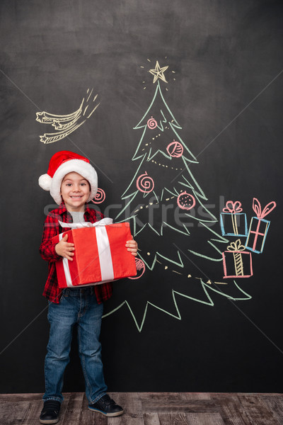 Happy child holding gift near Christmas tree drawing on chalkboa Stock photo © deandrobot